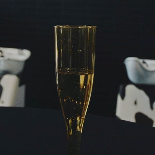 Champagne flute with gold liquid in front of a 'Rootbar' sign.