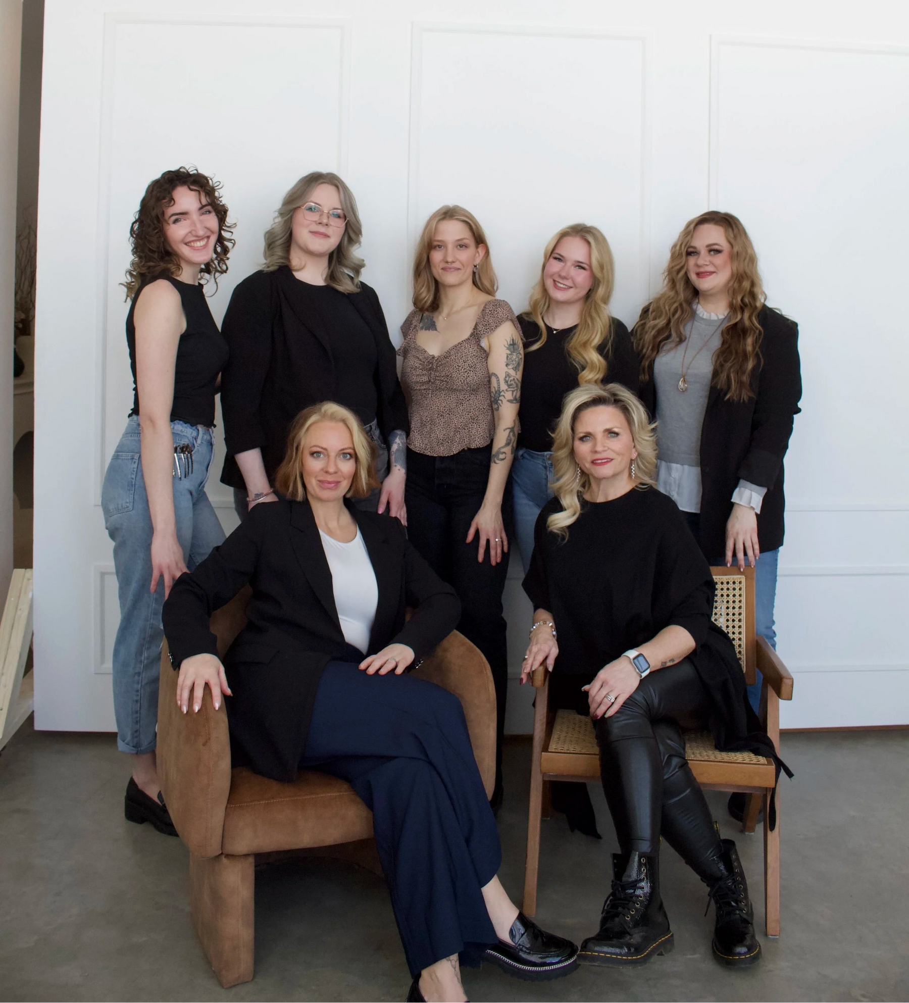 Group of women posing together in a studio setting with a white wall and wooden floor.