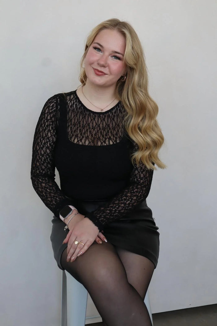 Woman wearing a black lace top and skirt with sheer tights against a plain background